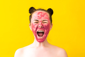 a girl of European appearance, with dark hair, on a yellow background screams. takes spa treatments. on the face a cosmetic mask. surprised and unhappy with her reflection