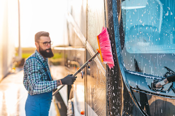 Young male worker washing bus.