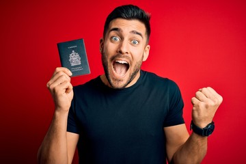 Young handsome tourist man holding canada canadian passport id over red background screaming proud...