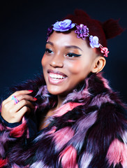 young pretty african american woman in spotted fur coat and flowers jewelry posing on black background