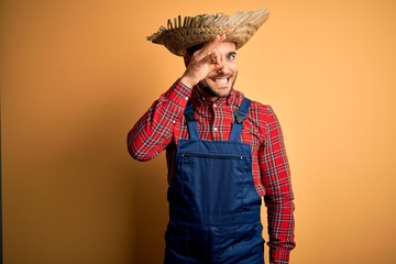 Young rural farmer man wearing bib overall and countryside hat over yellow background doing ok...