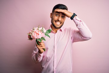 Young romatic man holding bouquet of spring flowers over pink isolatd background stressed with hand on head, shocked with shame and surprise face, angry and frustrated. Fear and upset for mistake.
