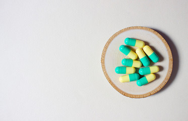 Green yellow pills or capsules stack freely on a wooden circle on a light background.