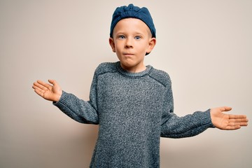 Young little caucasian kid with blue eyes wearing wool cap over isolated background clueless and...