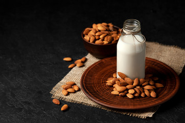 one bottle of almond milk on a dark black background with nuts, vegetarian milk without sugar and lactose