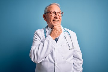 Senior grey haired doctor man wearing stethoscope and medical coat over blue background with hand on chin thinking about question, pensive expression. Smiling with thoughtful face. Doubt concept.