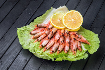 Boiled shrimp with lemon on a lettuce leaf. Beautifully laid out appetizer. Asian cuisine. Seafood on a dark wooden table.
