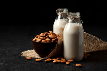 almond milk without sugar and lactose in bottles with sprinkled nuts, vegetarian milk drink on a black table