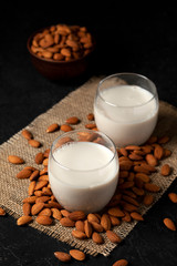 almond milk with glasses on sprinkled nuts, vegetarian milk drink without lactose against a dark background, close-up