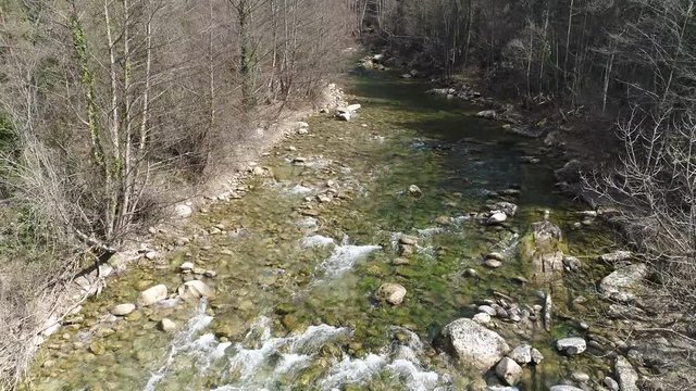 AERIAL DRONE 45 DEGREE CLOSE SHOT OF TRANSPARENT RIVER AND TREES IN WINTER