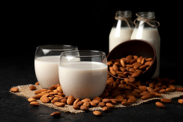 sugar-free and lactose-free almond milk in glasses and bottles with powdered nuts, vegetarian milk drink on a black table