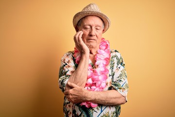 Grey haired senior man wearing summer hat and hawaiian lei over yellow background thinking looking tired and bored with depression problems with crossed arms.