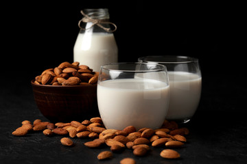 sugar-free and lactose-free almond milk in glasses and bottles with powdered nuts, vegetarian milk drink on a black table