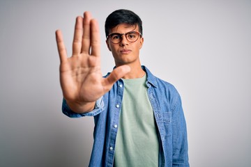 Young handsome man wearing casual shirt and glasses over isolated white background doing stop sing...