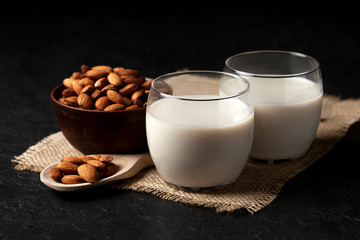 glass of almond milk without lactose and sugar with sprinkled nuts on a dark background, a veggie milk drink on a table