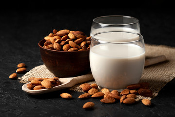almond milk without sugar and lactose in glass with sprinkled nuts, vegetarian milk drink on a dark black table