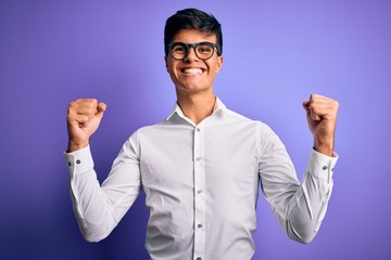 Young handsome business man wearing shirt and glasses over isolated purple background celebrating surprised and amazed for success with arms raised and open eyes. Winner concept.
