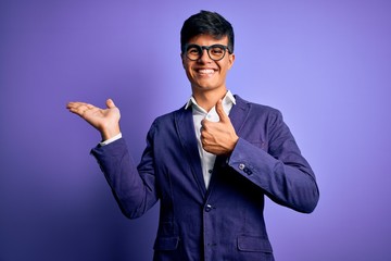 Young handsome business man wearing jacket and glasses over isolated purple background Showing palm hand and doing ok gesture with thumbs up, smiling happy and cheerful