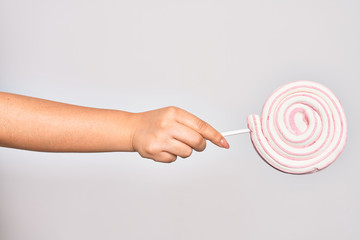 Hand of caucasian young woman holding sweet pink lollipop over isolated white background