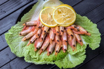 A plate of prawns on lettuce leaves and sliced lemon. Seafood on a dark wooden table.