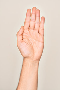 Hand of caucasian young man showing fingers over isolated white background stretching and reaching with open hand for handshake, showing palm