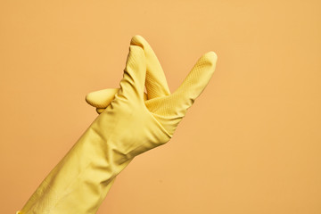 Hand of caucasian young man with cleaning glove over isolated yellow background snapping fingers...