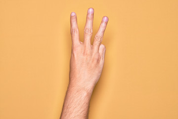 Hand of caucasian young man showing fingers over isolated yellow background counting number 3 showing three fingers