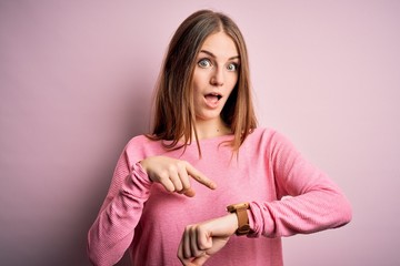 Young beautiful redhead woman wearing casual sweater over isolated pink background In hurry...