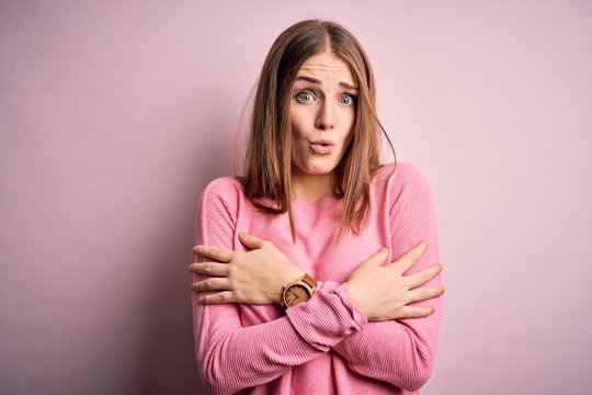 Young beautiful redhead woman wearing casual sweater over isolated pink background shaking and freezing for winter cold with sad and shock expression on face