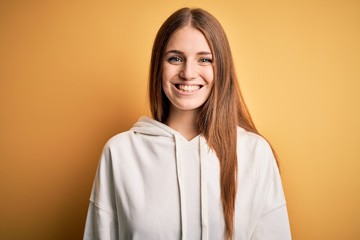 Young beautiful redhead sporty woman wearing sweatshirt over isolated yellow background with a happy and cool smile on face. Lucky person.