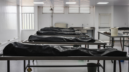 Covered human corpses on tables in a morgue / mortuary waiting for identification, autopsy, burial or cremation. Taken in Armenia, Colombia. - obrazy, fototapety, plakaty