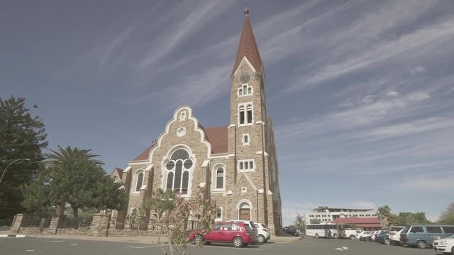 Panning shot of plants against church in city on sunny day, vehicles near religious building against sky - Windhoek, Namibia