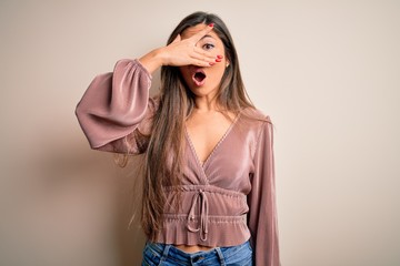 Young beautiful brunette elegant woman with long hair standing over isolated background peeking in shock covering face and eyes with hand, looking through fingers with embarrassed expression.
