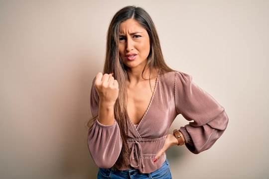 Young beautiful brunette elegant woman with long hair standing over isolated background angry and mad raising fist frustrated and furious while shouting with anger. Rage and aggressive concept.