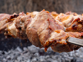 Juicy and fresh slices of pork meat are strung on skewers and grilled in charcoal grill. Fragrant smoke. Natural meat dish outdoors on a spring day.