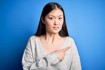 Young beautiful asian woman wearing casual sweater standing over blue isolated background Pointing...