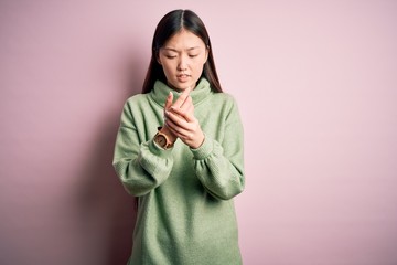 Young beautiful asian woman wearing green winter sweater over pink solated background Suffering...