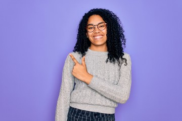 Young african american woman wearing casual sweater and glasses over purple background cheerful with a smile on face pointing with hand and finger up to the side with happy and natural expression