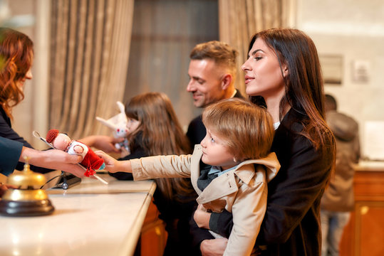 Giving a reason to smile. Happy family checking in hotel at reception desk. Receptionist is giving a toy for a boy while welcoming guests at the hotel. - Powered by Adobe