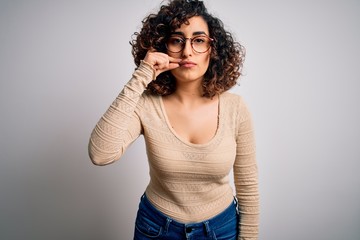 Young beautiful curly arab woman wearing casual t-shirt and glasses over white background mouth and lips shut as zip with fingers. Secret and silent, taboo talking