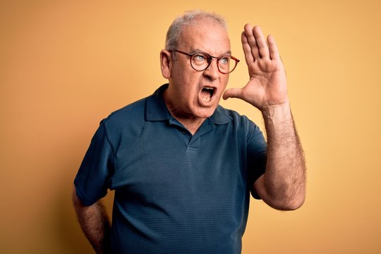 Middle age handsome hoary man wearing casual polo and glasses over yellow background shouting and screaming loud to side with hand on mouth. Communication concept.