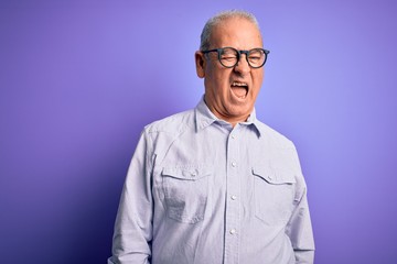 Middle age handsome hoary man wearing striped shirt and glasses over purple background winking looking at the camera with sexy expression, cheerful and happy face.