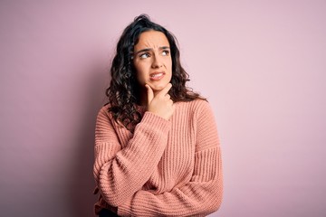 Fototapeta premium Young beautiful woman with curly hair wearing casual sweater over isolated pink background Thinking worried about a question, concerned and nervous with hand on chin