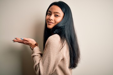 Young beautiful chinese woman wearing casual sweater over isolated white background pointing aside with hands open palms showing copy space, presenting advertisement smiling excited happy