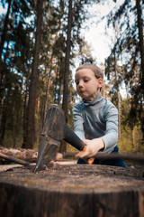 Young boy lumberjack chopping wood. Child with an axe in forest. Dynamic ax cutting of branch, logging. Son of Forester. Man raising boy. Hiking with children in nature. Danger of injury to child