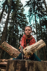 Young strong girl teenager chopping wood with axe blow in forest. Purposeful ambitious girl with male character. Hiking, camping and wild travel. Lumberjack woman cuts firewood for bonfire