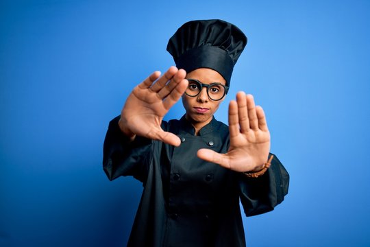 Young african american chef woman wearing cooker uniform and hat over blue background doing frame using hands palms and fingers, camera perspective