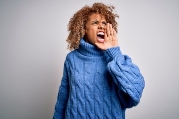 Young beautiful african american woman wearing turtleneck sweater over white background shouting and screaming loud to side with hand on mouth. Communication concept.