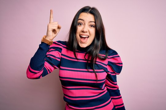 Young brunette elegant woman wearing striped shirt over pink isolated background pointing finger up with successful idea. Exited and happy. Number one.