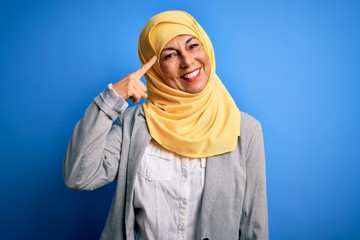 Middle age brunette business woman wearing muslim traditional hijab over blue background Smiling pointing to head with one finger, great idea or thought, good memory